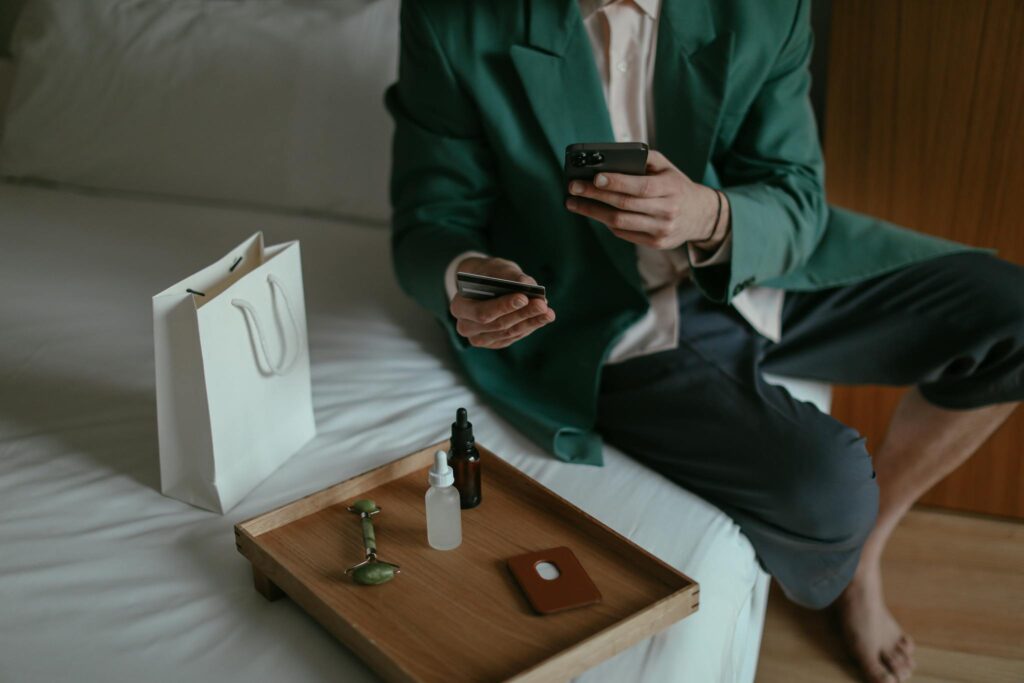 Anonymous man using smartphone while placing order with credit card sitting near cosmetic products