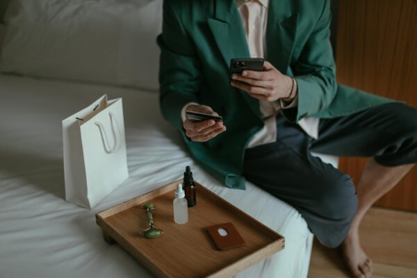 Anonymous man using smartphone while placing order with credit card sitting near cosmetic products